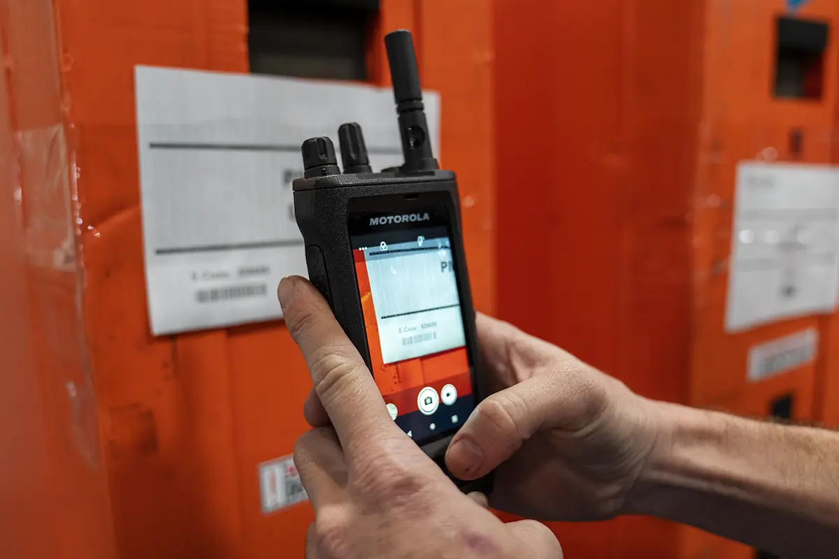 Person holding a Motorola DMR device in front of an orange background with labels, scanning or reading information.