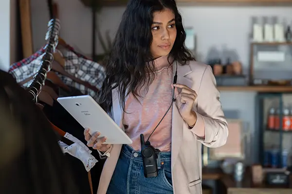 Person adjusting Motorola wireless earpiece while holding tablet in retail environment