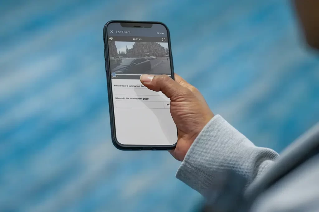Person holding a smartphone with an app open showing an incident summary and location entry screen.
