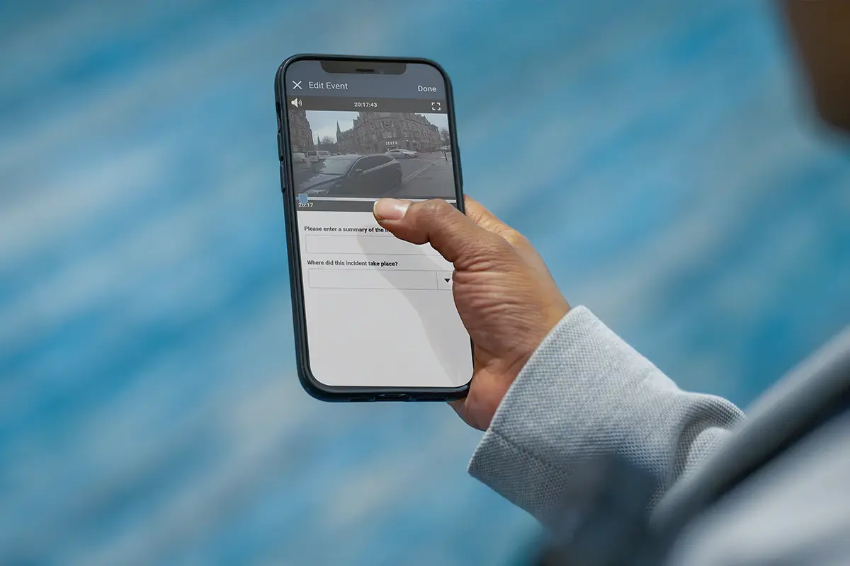 Person holding a smartphone with an app open showing an incident summary and location entry screen.