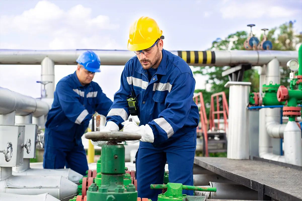 Utility workers operating valve at industrial site with visible pipes and equipment