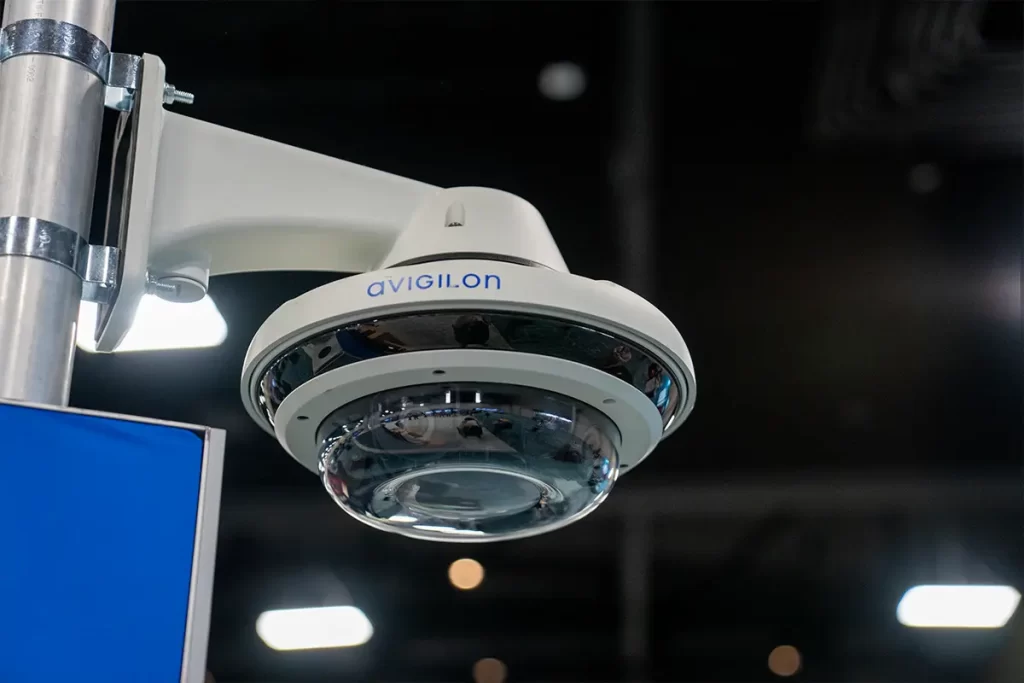 Avigilon dome-shaped fixed camera mounted on a pole in an indoor setting with visible lighting.