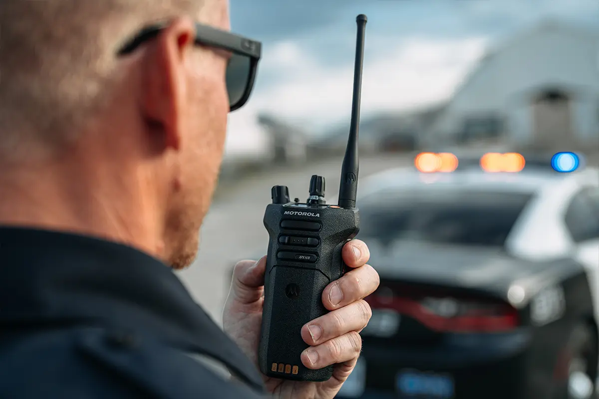 Emergency responder holding Motorola two-way radio near police vehicle with lights activated