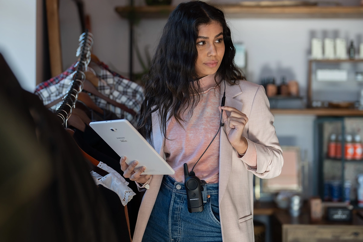 A retail worker holding a tablet with a two-way radio clipped to their jeans, representing Logic Technologies’ role in delivering Motorola Solutions technology through a trusted dealer network.