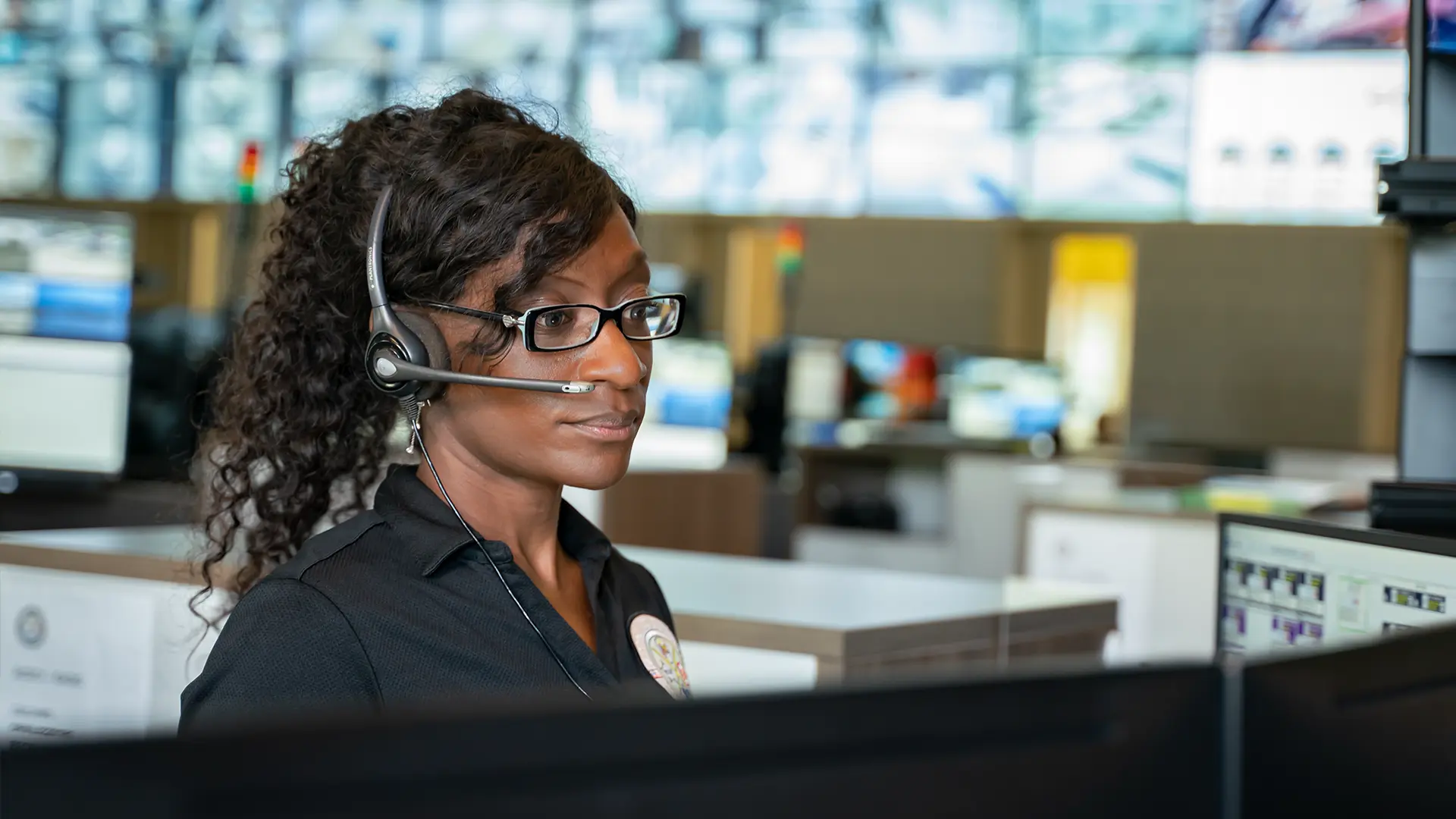 Person wearing a headset in a control room or call centre with multiple monitors displaying operational data.