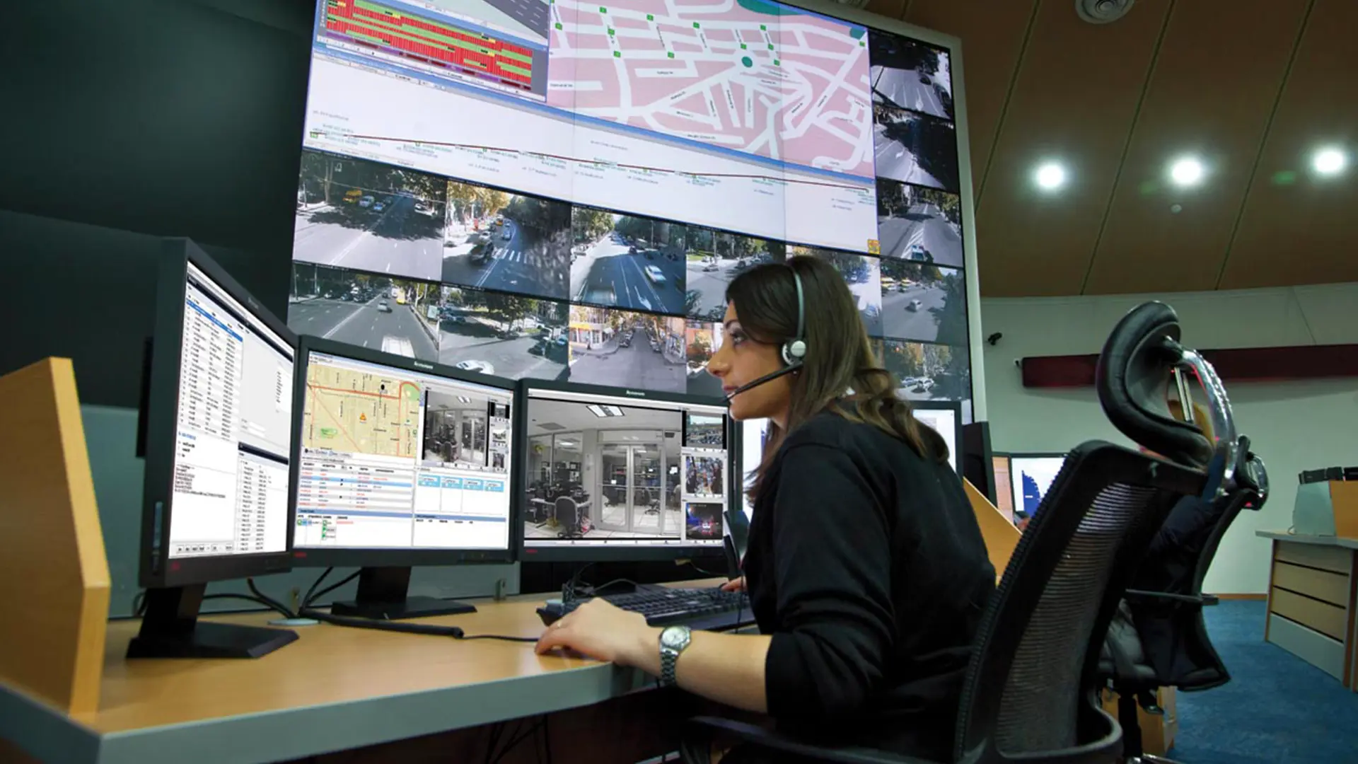 A control station operator monitors multiple screens displaying surveillance footage and maps, illustrating Motorola Solutions’ integrated software platform in action.