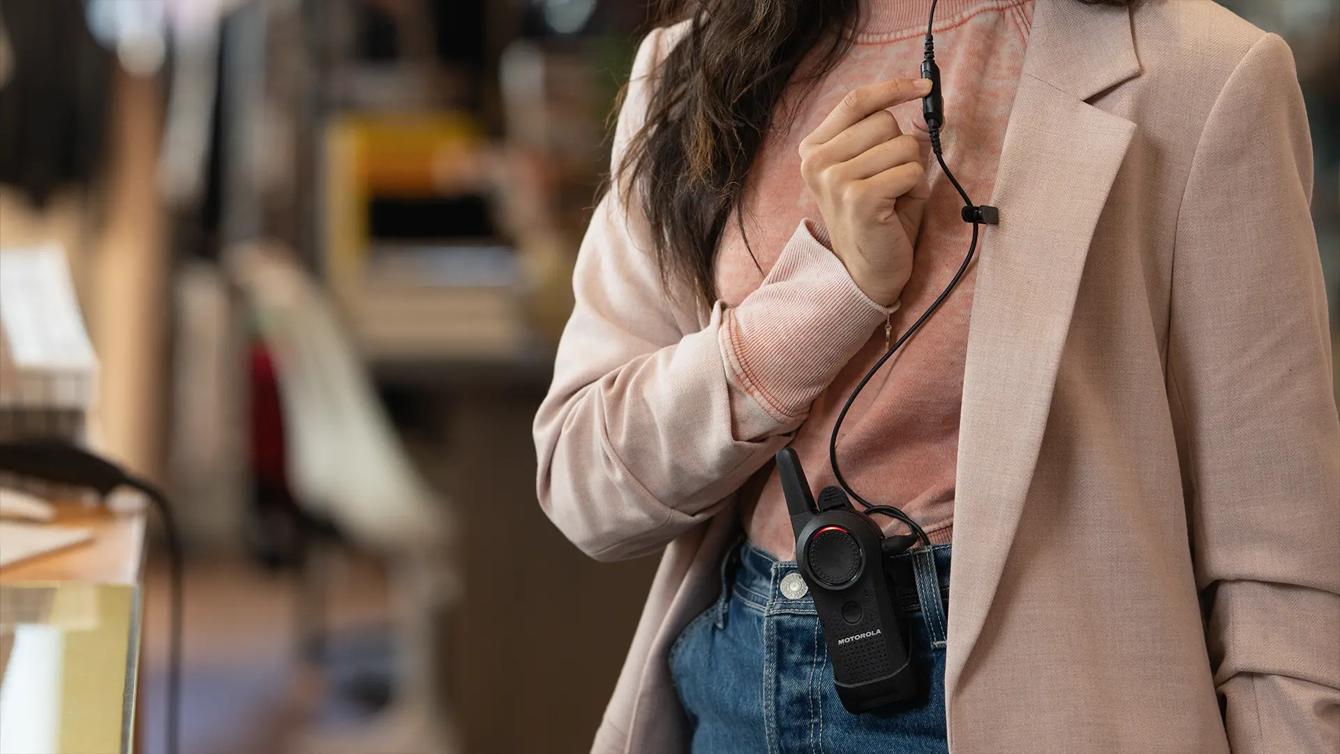 Retail worker uses a Motorola Solutions Curve business radio with attached earpiece to contact other team members.